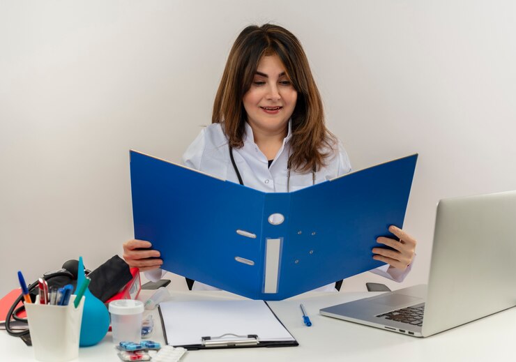 impressed-middle-aged-female-doctor-wearing-medical-robe-stethoscope-sitting-desk-with-medical-tools-clipboard-laptop-holding-looking-folder-isolated_141793-69165